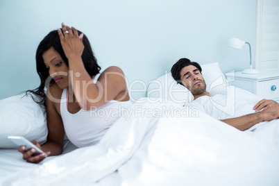 Woman checking her mobile phone while man sleeping on bed