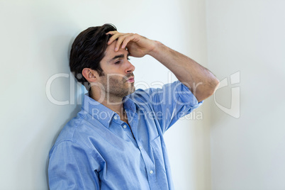 Depressed man with hand on forehead leaning against a wall