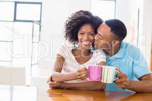 Man kissing woman while toasting coffee mug