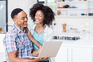 Happy young couple using laptop in kitchen