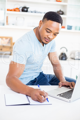 Young man using laptop while writing in diary
