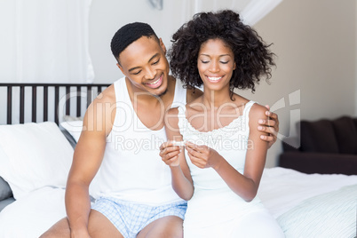 Happy couple looking at pregnancy test on bed