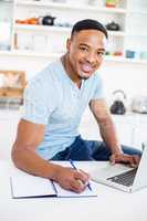 Young man using laptop while writing in diary