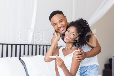 Happy couple with pregnancy test on bed