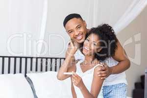 Happy couple with pregnancy test on bed