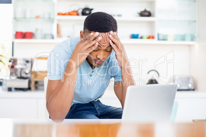 Tense young man sitting in kitchen with laptop