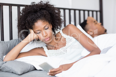 Young woman using mobile phone while man sleeping on bed
