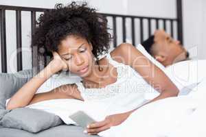 Young woman using mobile phone while man sleeping on bed