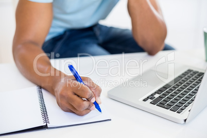 Mid section of a man with laptop writing in diary