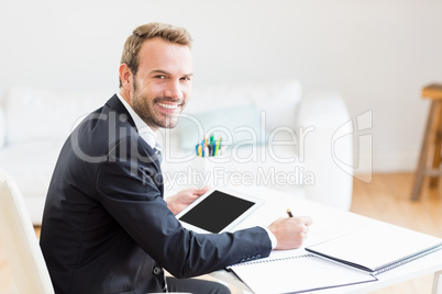 Businessman writing in a diary and using a digital tablet