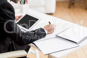 Businessman writing in a diary and using a digital tablet