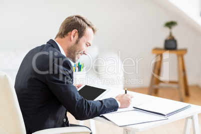 Businessman writing in a diary and using a digital tablet