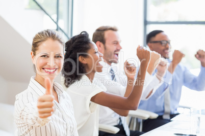 Businesswoman showing her thumbs up while team celebrating in ba