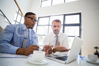 Businessmen looking at laptop and interacting in office