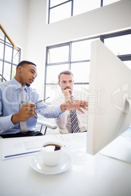 Businessmen looking at computer and interacting in office