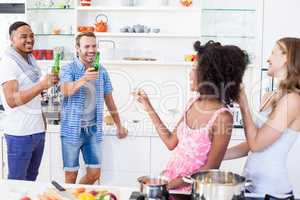 Friends toasting beer and wine in kitchen