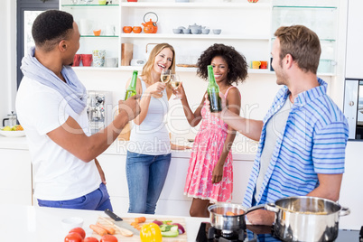 Friends toasting beer and wine in kitchen