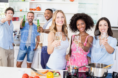 Friends toasting beer and wine glasses in kitchen