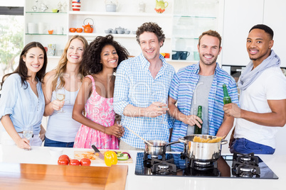 Friends holding beer bottles and glasses of wine in kitchen