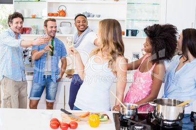 Friends toasting beer and wine glasses in kitchen