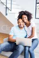 Happy couple sitting on steps and using laptop