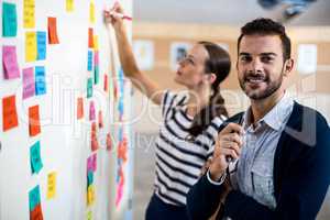 Young man smiling at camera while colleague writing on white boa