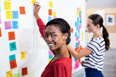 Young woman smiling at camera while writing on white board
