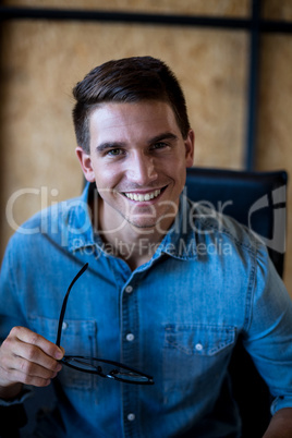 Young man holding spectacles smiling at camera