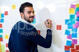 Young man smiling at camera while writing on white board