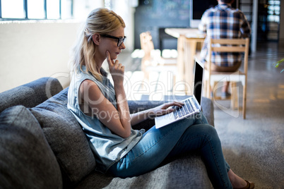 Young woman sitting on sofa using laptop