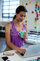 Young woman holding coffee cup and using laptop
