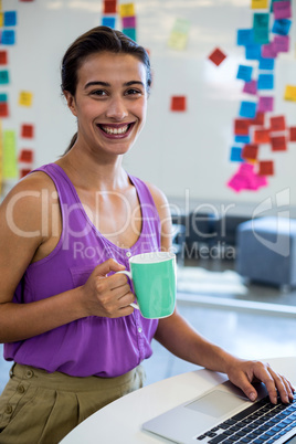 Young woman holding coffee cup and using laptop