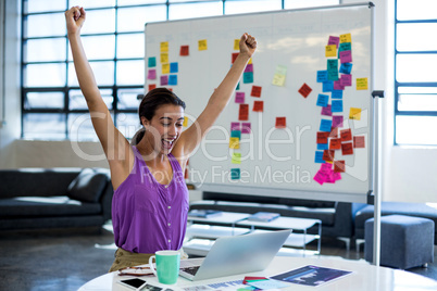 Excited woman sitting on table with digital tablet and laptop