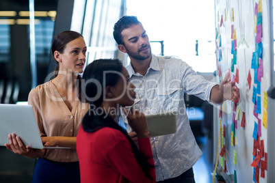 Team of colleagues standing by white board reading sticky notes