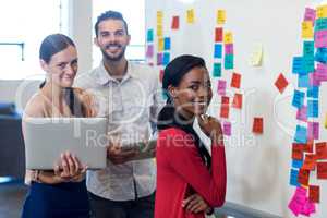 Team of colleagues standing by white board holding digital table