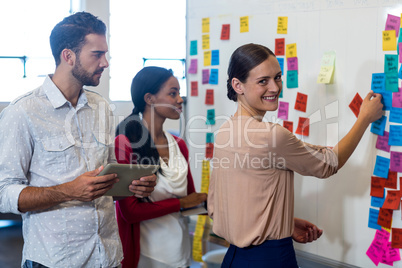 Team of colleagues standing by white board reading sticky notes