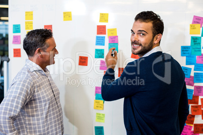 Young man smiling at camera while writing on the white board whi