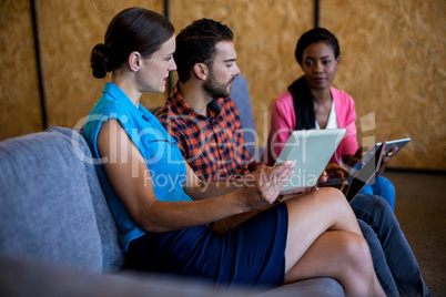 Colleagues using digital tablet and laptop while sitting on sofa