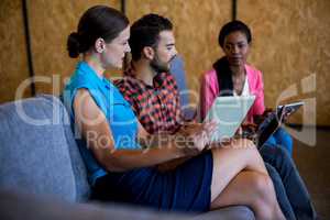 Colleagues using digital tablet and laptop while sitting on sofa