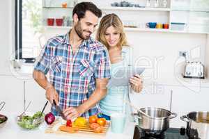Young couple chopping vegetable and using digital tablet