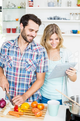 Young couple chopping vegetable and using digital tablet