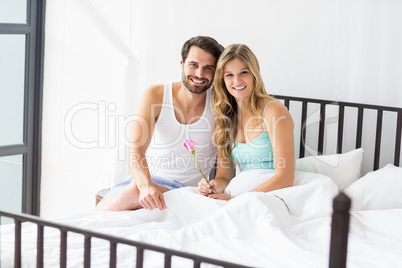 Young couple holding a flower sitting on a bed