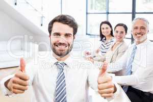 A businessman is putting his thumbs up and behind him his collea