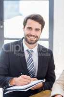 A businessman is posing, smiling and holding a pen and a book