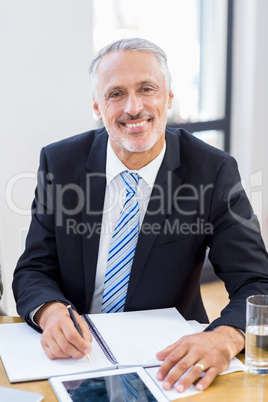 A businessman is sitting in front of his office, smiling and pos