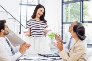 A woman is standing, smiling and talking to her colleagues who a