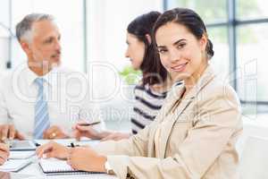 Businesswoman smiling at camera while colleagues discussing