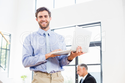 A businessman is holding his laptop and smiling