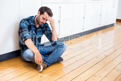Tensed man with hand on forehead sitting on wooden floor