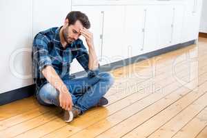 Tensed man with hand on forehead sitting on wooden floor